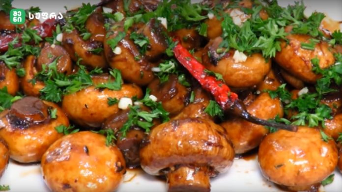 Shiny glazed roasted baby potatoes garnished with chopped parsley and a red chili pepper in a brown sauce.