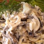 Creamy mushroom and cheese pasta salad in a clear glass bowl, topped with a dill sprig.