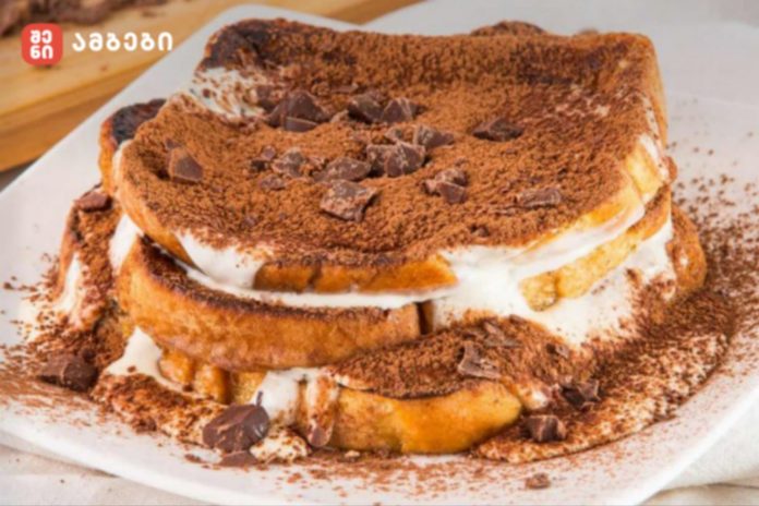 Layered tiramisu-style dessert with cream between bread slices, cocoa powder and chocolate chunks on top