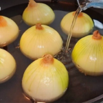 Onions boiling in a pot of water on a stove, their yellowish skins visible above the liquid level.