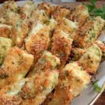 Plate of golden-brown breaded fried pieces with herbs, served with a creamy dipping sauce on the side and parsley garnish.
