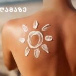Sun-shaped sunscreen design on a model's shoulder at the beach, with a yellow logo and Georgian text in the top-left corner.