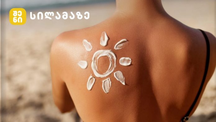 Sun-shaped sunscreen design on a model's shoulder at the beach, with a yellow logo and Georgian text in the top-left corner.