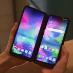 Two smartphones in a dual‑screen foldable case, held in each hand, displaying vibrant colorful home screens with app icons.