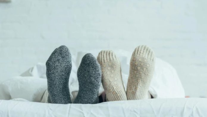 Person lying in bed with gray and beige knitted socks peeking out from under a white duvet.