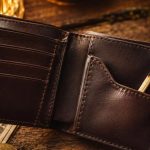 Open brown leather wallet on a wooden surface with cash visible and a burnt match tucked into the inner pocket; warm lighting.