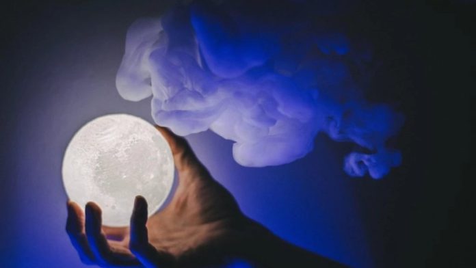 Hand cradling a glowing full-moon orb against a dark blue smoky background.