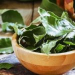 Fresh bay leaves in a wooden bowl resting on a rustic wooden surface.