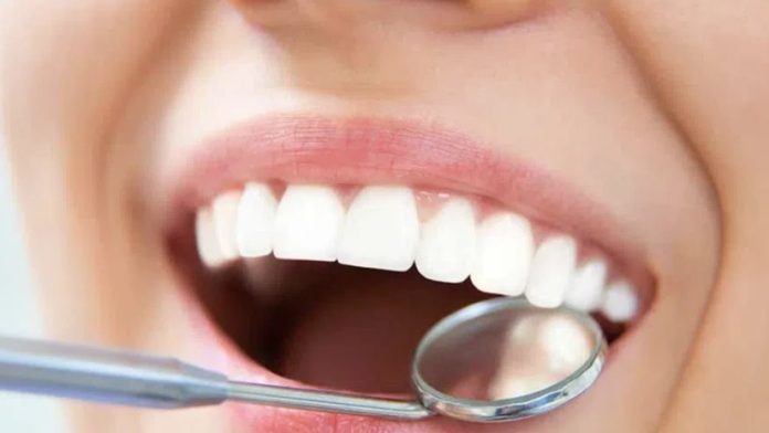 Close-up of a mouth during a dental checkup, showing white teeth and a dental mirror inside the open mouth.