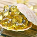 Seashell filled with yellow softgel capsules on a woven mat, suggesting fish oil capsules.