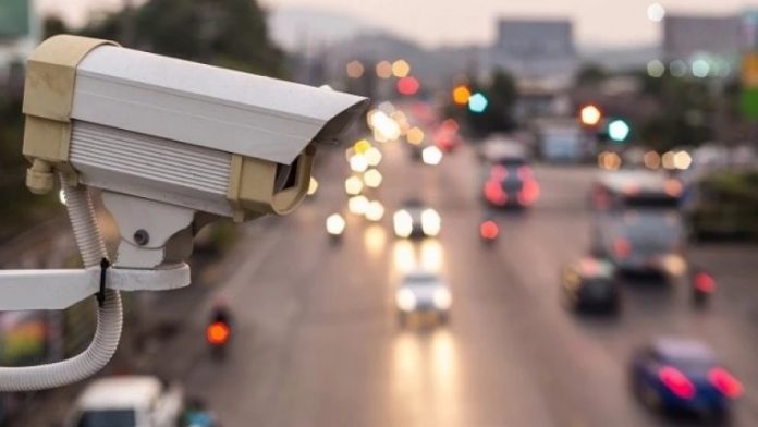 Surveillance camera overlooking a busy multi-lane highway with blurred car lights at dusk.
