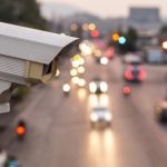 Traffic surveillance camera monitoring a busy highway with blurred car headlights in the background.
