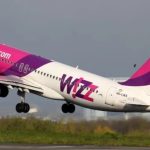 Wizz Air jet taking off from the runway with pink and purple livery in ascent.