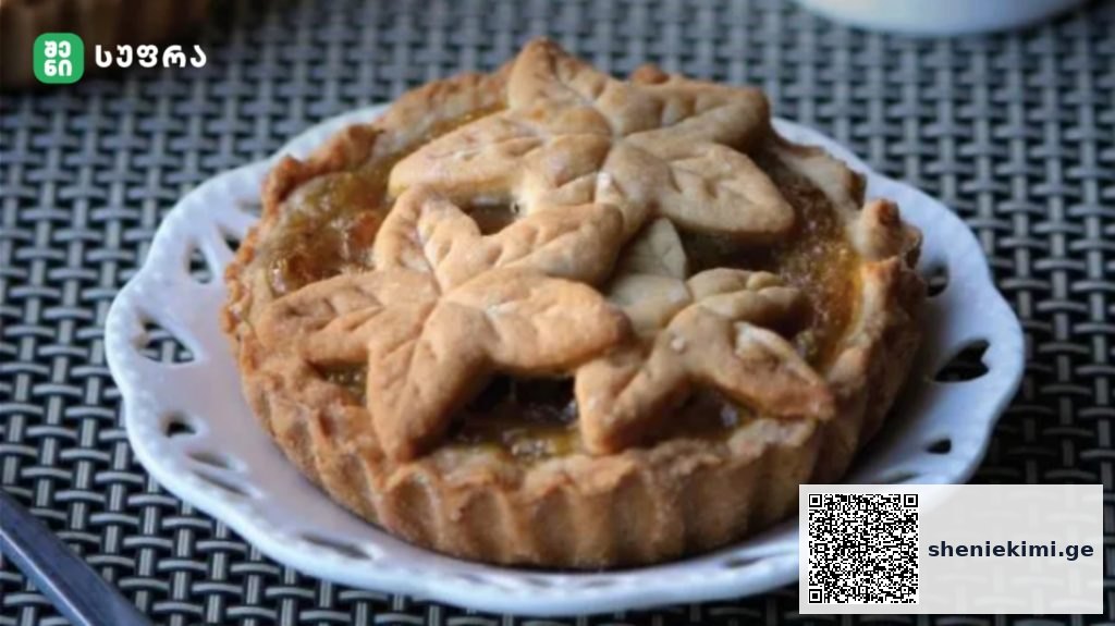 Decorative fruit tart with leaf-shaped pastry crust on a white plate, sitting on a woven table surface.