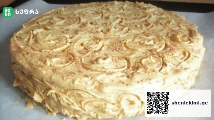 Round cake with white frosting and piped rosette decorations on top and along the sides, resting on parchment.