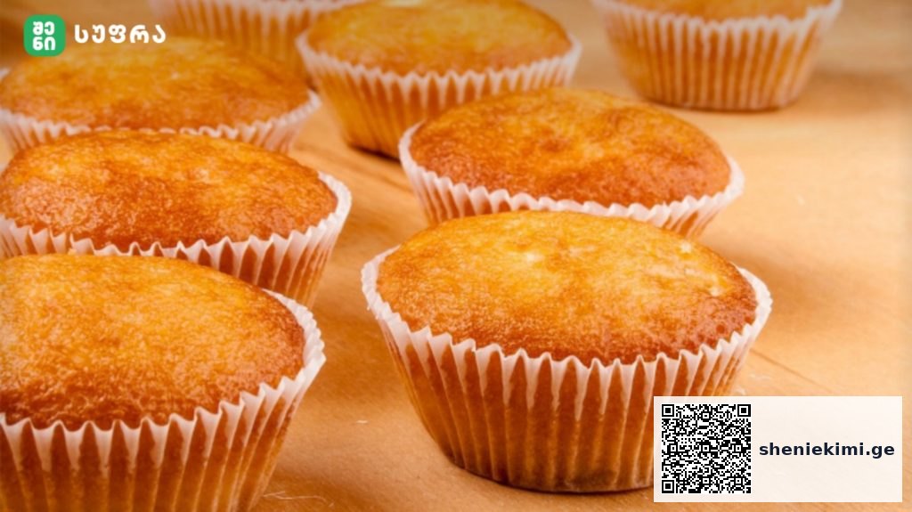 Golden muffins in white paper cups resting on a wooden countertop, fresh and warm.
