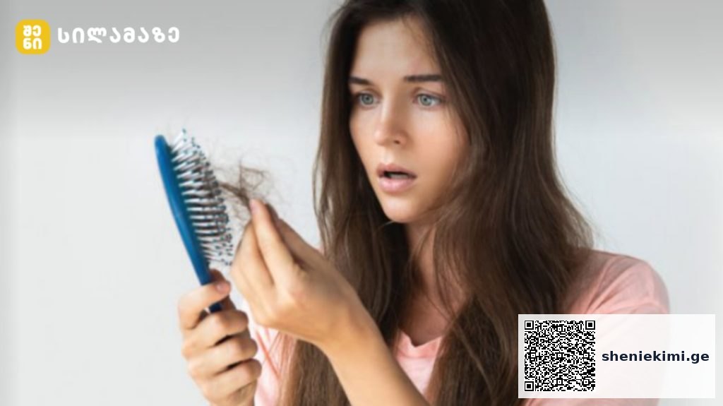 Woman with long brown hair holds a blue hairbrush and inspects strands of hair in her hand, looking surprised or worried.