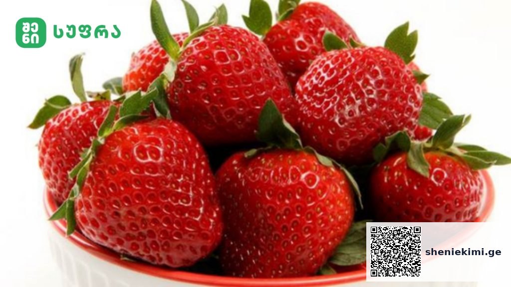 Fresh strawberries piled in a red bowl, with a green logo in the top-left corner.
