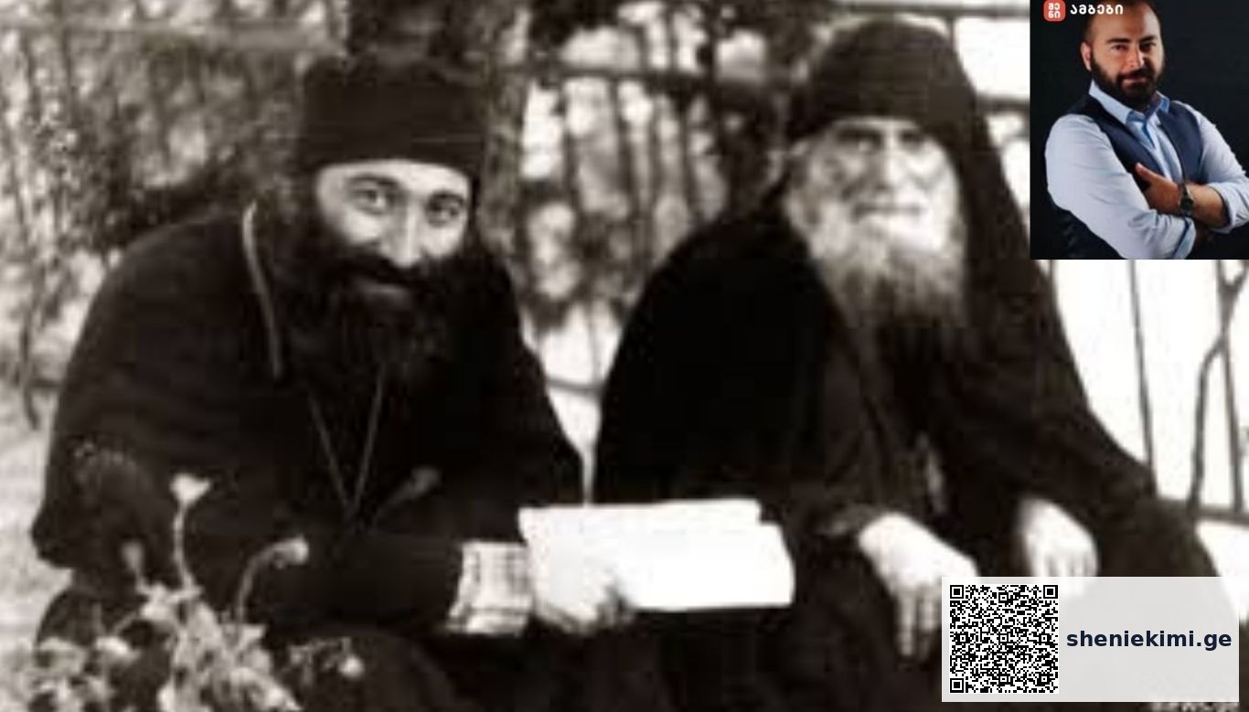 Two bearded monks in dark robes sitting outdoors, one holding a letter