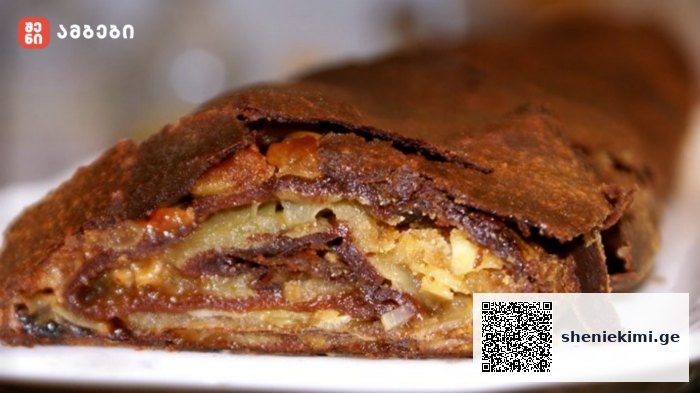 Close-up of a nut-filled pastry slice with a flaky, chocolate-dusted crust on a white plate