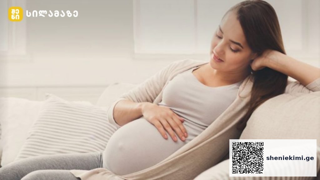 Pregnant woman relaxing on sofa, cradling her baby bump and smiling at home.