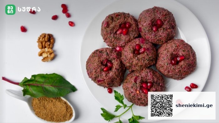 Plate of round beetroot patties topped with pomegranate seeds on a white platter with greens and spices nearby