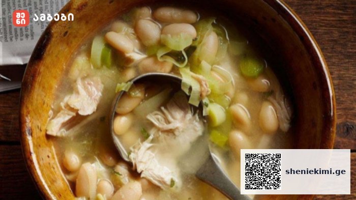 Bowl of white bean and shredded chicken soup with green onions in a wooden bowl and a spoon.