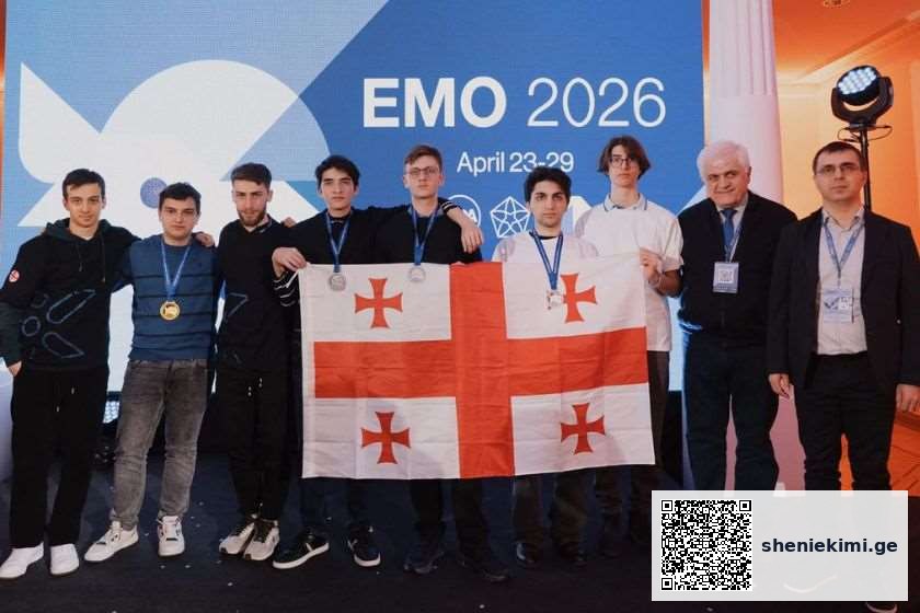 Group of young men on stage holding a Georgian flag with medals at EMO 2026 event, backdrop reads EMO 2026 April 23-29.