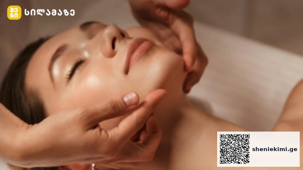 Close-up of a woman receiving a facial massage, eyes closed, as a therapist gently supports her jaw and cheekbones