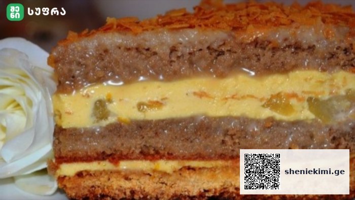Layered cake with yellow custard filling and orange topping, displayed on a plate beside a white flower garnish.