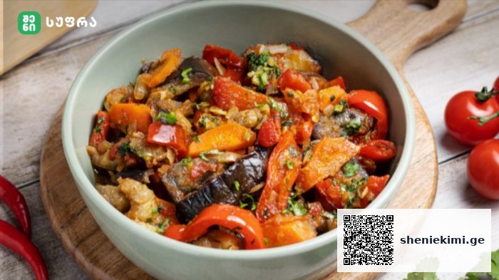 Bowl of colorful sautéed vegetables (eggplant, red and orange peppers, tomatoes) garnished with herbs on a wooden board.