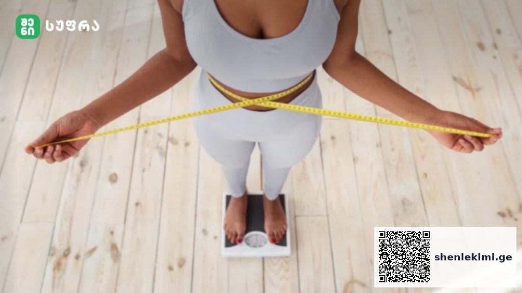 Top-down view of a person measuring their waist with a yellow tape while standing on a scale on a wooden floor.