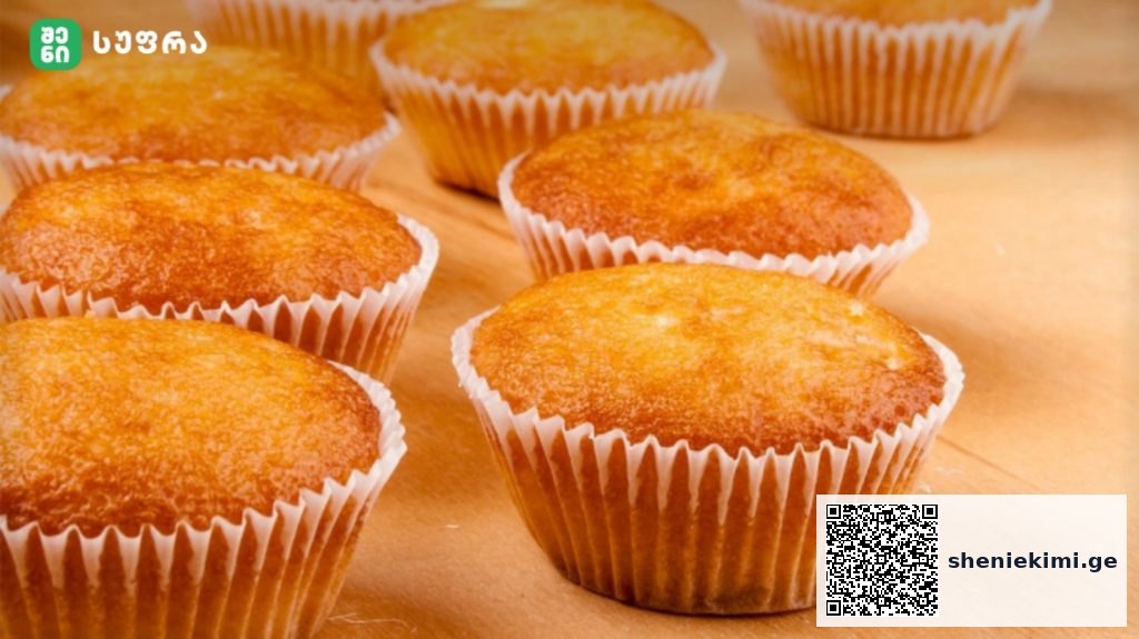 Golden muffins in white paper cups resting on a wooden countertop, fresh and warm.