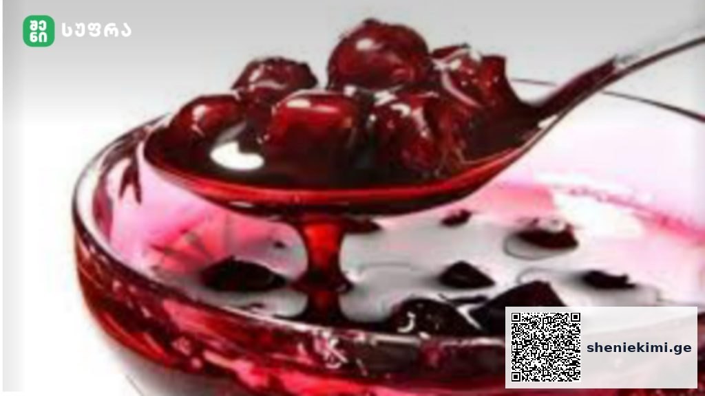 Clear glass bowl filled with bright red juice and dark fruit pieces, likely cherries, on a pale background.