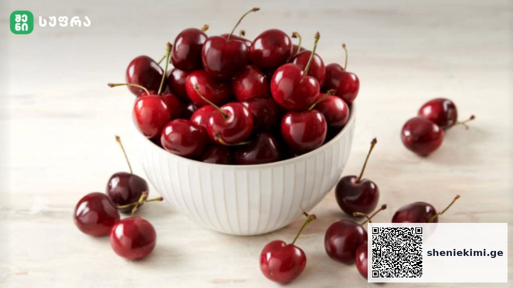 White ceramic bowl brimming with ripe red cherries on a light wooden surface disabling the cluttered background, fresh and glossy.