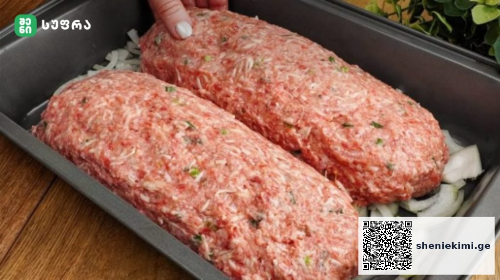 Two raw seasoned ground beef loaves in a pan over chopped onions, ready to bake, with herbs visible in the meat mixture