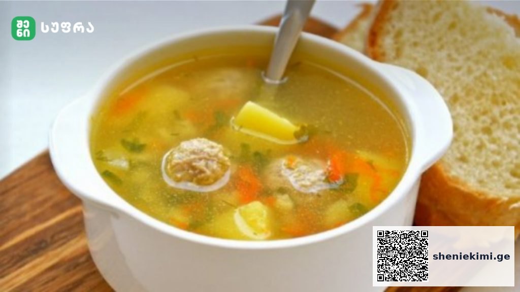 White ceramic bowl of vegetable soup with carrots, potatoes and herbs, served with slices of bread on a wooden board.