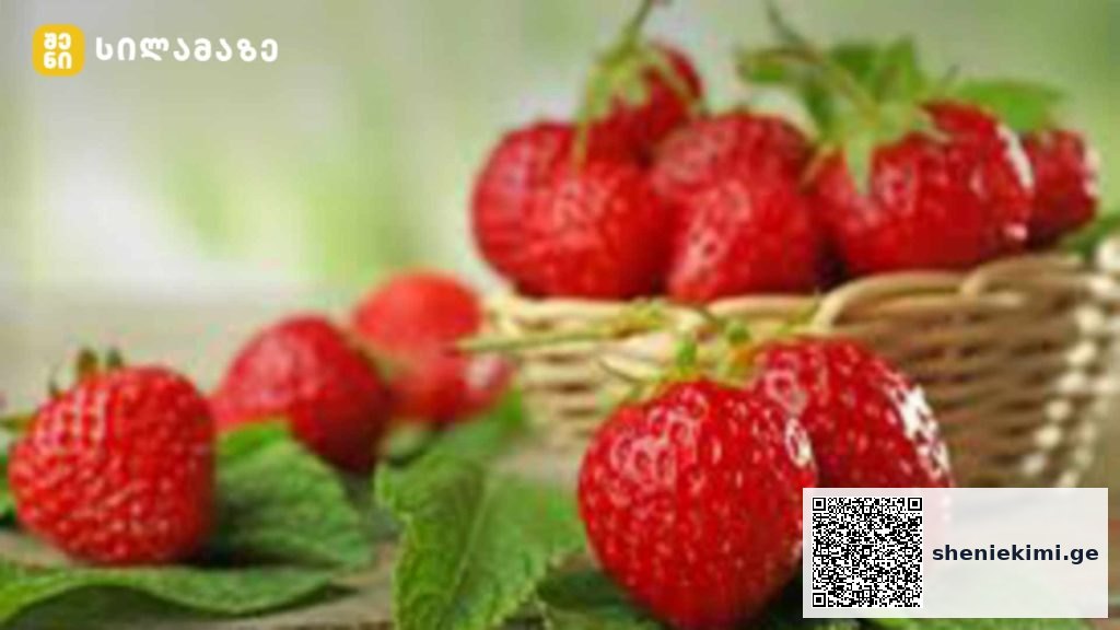 Fresh ripe strawberries in a wicker basket on a wooden surface, green garden background.