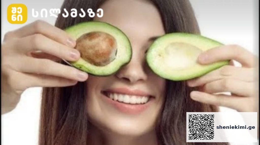 Young woman holding avocado halves over her eyes and smiling playfully.