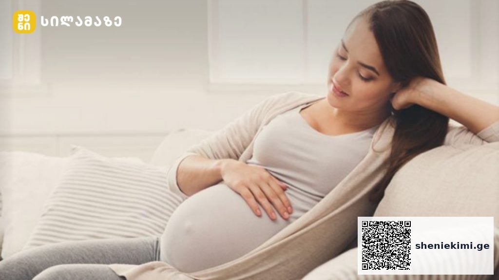 Pregnant woman relaxing on sofa, cradling her baby bump and smiling at home.