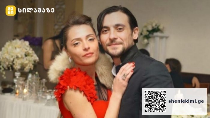 Couple posing together at a formal event; woman in a red dress with a fur stole and the man in a dark suit, background shows a table with flowers and candles.