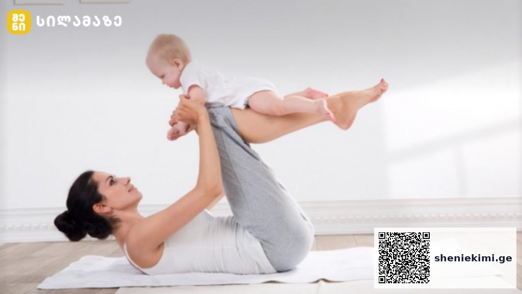 Mother lying on a white mat while lifting her baby overhead with legs raised in a calm, sunlit room.