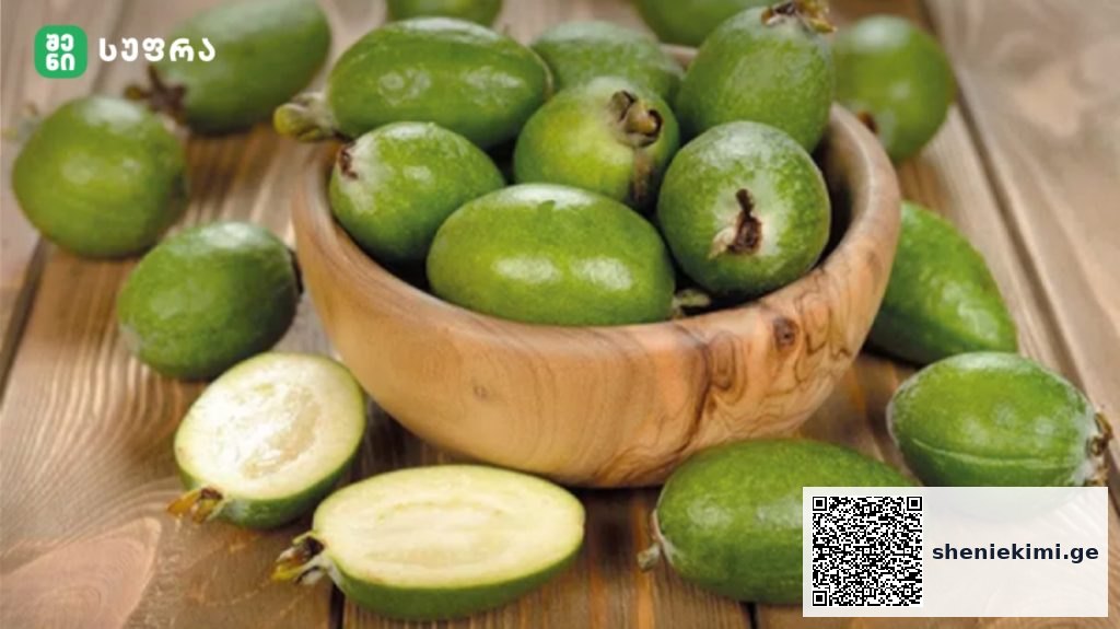 Green feijoa fruits in a wooden bowl on a rustic wooden table, one cut open to show pale flesh inside.
