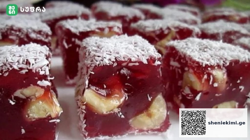 Red jelly dessert squares with banana pieces inside, coated in shredded coconut, arranged on a tray.