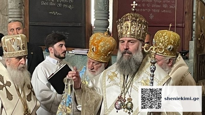 Orthodox bishops in ornate white and gold vestments during a ceremony, central figure holding a ceremonial staff.