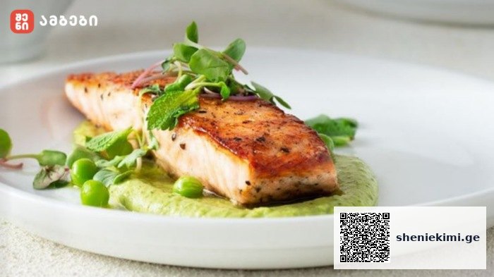 Pan-seared salmon fillet on a green pea-mint sauce with peas and microgreens on a white plate.