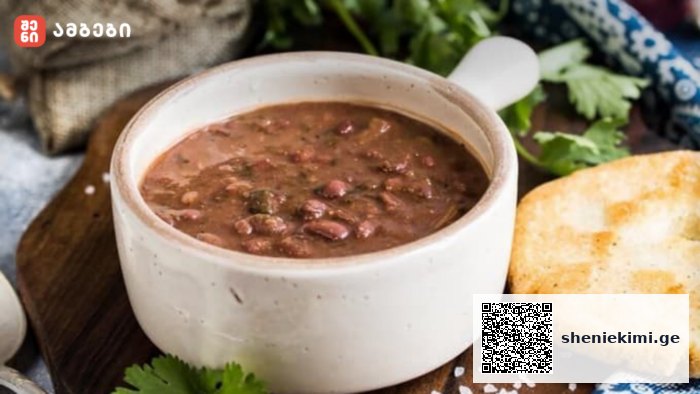 White ceramic bowl of hearty bean soup with a toasted bread slice on a wooden board, garnished with parsley.