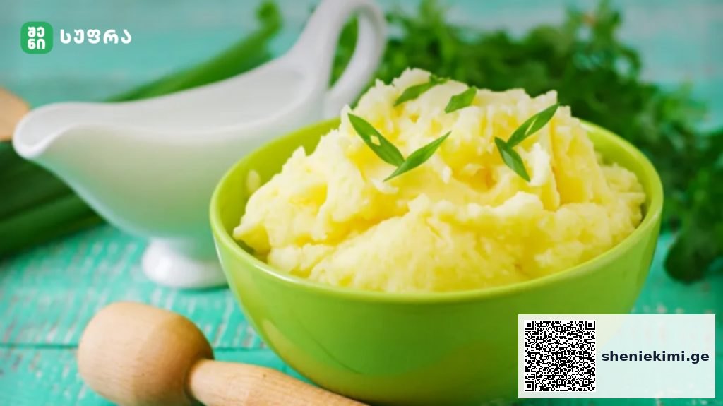 Green bowl of creamy mashed potatoes garnished with chives on a turquoise wooden table.