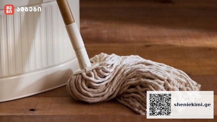 Cotton mop head resting on a wooden floor beside a white bucket, ready for cleaning transport scene.