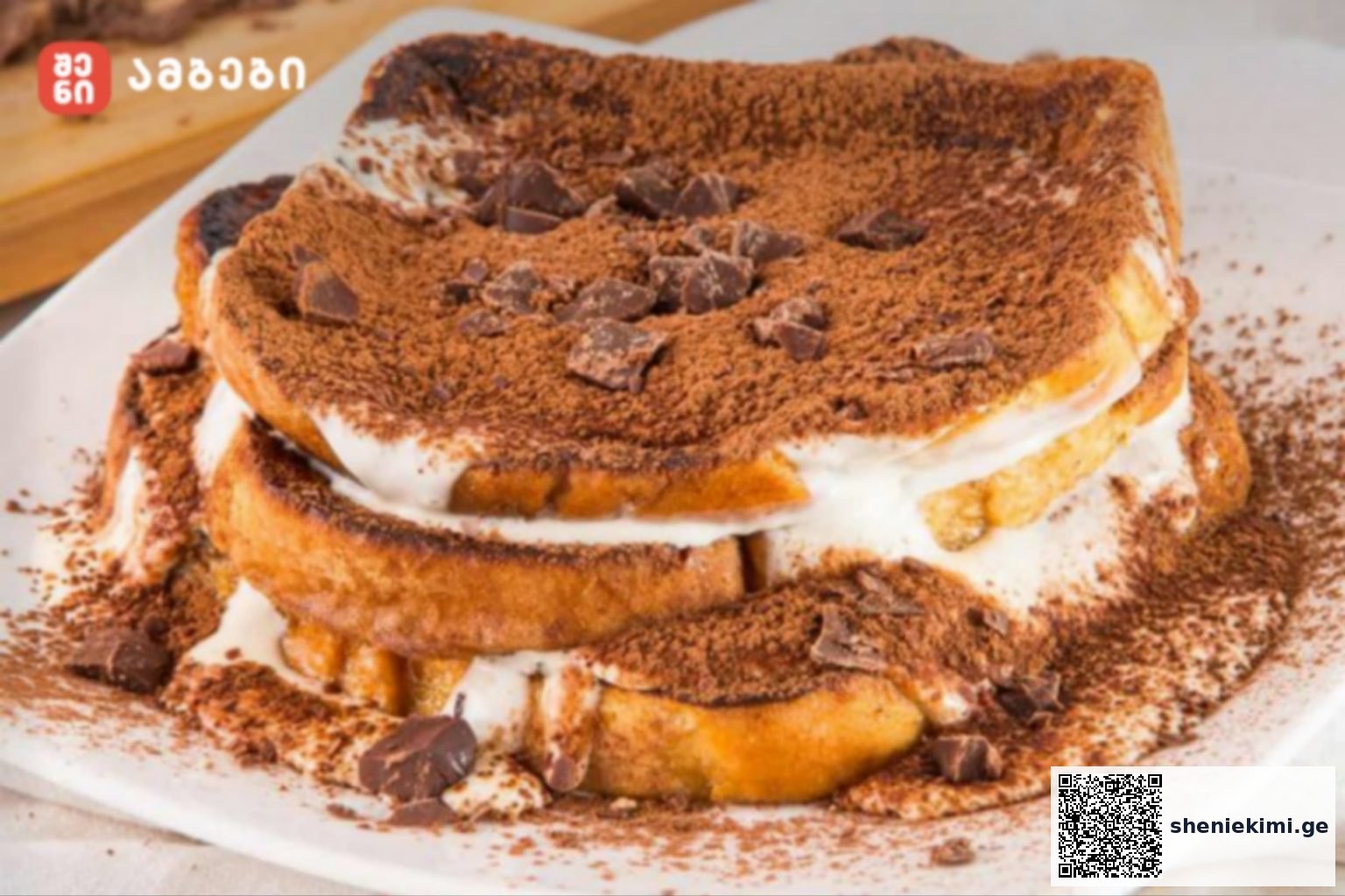 Layered tiramisu-style dessert with cream between bread slices, cocoa powder and chocolate chunks on top